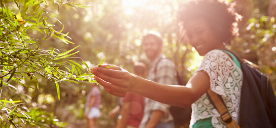 Woman in outdoors setting touching a plant and smiling